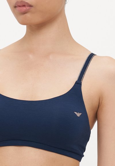 Navy plavi bralette napravljen od mekog materijala, s tankim trakama s bijelim detaljima i malim logom s lijeve strane blizu grudi.