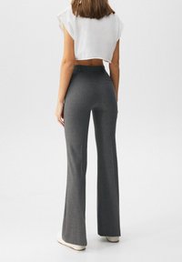 Grijze uitlopende broek met een op maat gemaakte pasvorm en zichtbare naaddetails. Gedragen met een cropped witte top en gecombineerd met witte schoenen.