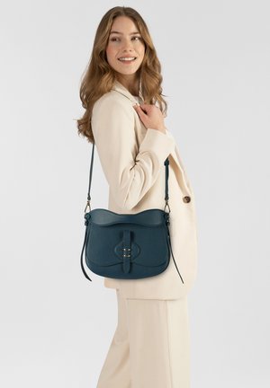 Bolso de hombro de cuero verde azulado oscuro con un diseño curvo, cierre frontal con correa y detalles en hardware dorado. Incluye correa de hombro ajustable.