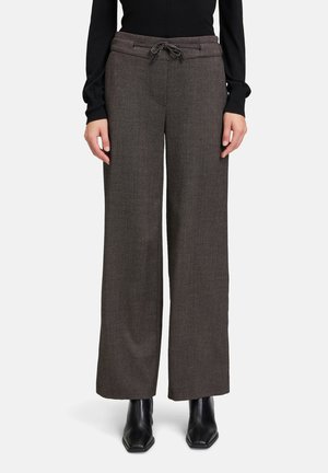 Wijdbenige broeken van een gestructureerde donkerrubberen stof, met een drawstring tailleband en subtiele patroon details. Zwarte enkellaarsjes accentueren de outfit.