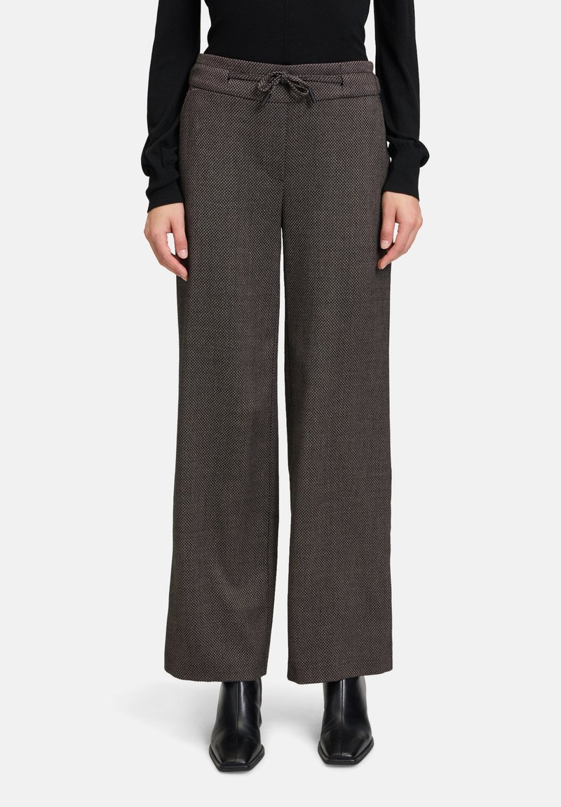 Bequeme weit geschnittene Hosen aus einem strukturierten dunkelbraunen Stoff, mit einem Kordelzugbund und subtilen Muster-Details. Schwarze Knöchelstiefel runden das Outfit ab.