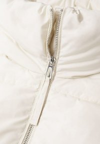 Pufferjack in off-white met een hoge kraag en zilveren rits. Heeft een quilted textuur en een gladde stof. Rits loopt verticaal.