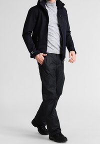 Marinblå softshell-jacka, grå polo, svarta cargobyxor och mörka sneakers. Tyget verkar slätt, med funktionella fickor och blixtlås.