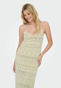 Rochie tricotată de culoare crem, cu o siluetă ajustată, bretele subțiri și un model complicat de dantelă deschisă, având designuri geometrice în întreaga sa compoziție.