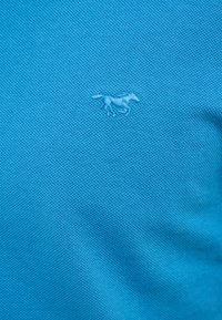 Blauer, strukturierter Stoff mit einem kleinen, gestickten Pferde-Motiv. Das Material wirkt atmungsaktiv und eignet sich für legere Bekleidung.