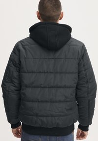 Giubbotto imbottito nero con design a trapunta e cappuccio nero removibile. I polsini e l'orlo a costine aumentano il comfort e la vestibilità.