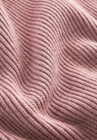 Tissu tricoté rose doux avec une texture côtelée montrant en gros plan des crêtes parallèles surélevées et des plis.