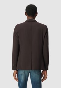 Brązowa marynarka w prążki z jednym rozcięciem, długimi rękawami i zapięciem na guziki, zestawiona z niebieskimi dżinsami. Gładka tekstura materiału.