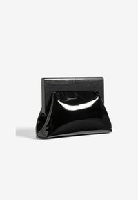 Čierna lakovaná kožená kabelka typu clutch s obdĺžnikovým čiernym dreveným rámom na uzatvorenie, stojaca vzpriamene na bielom pozadí.