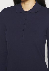 Mörkblå långärmad pikétröja med klassisk krage, knappslå fram och ett slätt, texturerat tyg.