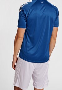 Modrý sportovní dres s krátkými rukávy, který má hladkou texturu. Bílé šortky s jemným vzorem chevron na bocích.