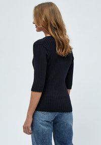 Schwarzes, geripptes Strickoberteil mit Dreiviertelärmeln und tailliertem Schnitt. Der Stoff weist vertikale Streifen für Textur und Form auf.