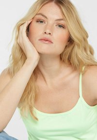 Mintgrünes Top mit dünnen Trägern, gefertigt aus einem strukturierten Stoff. Das Model hat lange, wellige blonde Haare und einen natürlichen Make-up-Look.