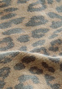 Tkanina s leopardím vzorem s texturovaným, tkaným vzorem v béžových a tmavě hnědých tónech, s křivkovými tvary a výraznými barevnými variacemi.