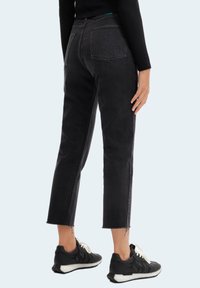 Vaqueros de mezclilla negra con corte recto, recortados a la altura del tobillo, con dobladillos deshilachados y dos bolsillos traseros, acompañados de zapatillas deportivas negras.