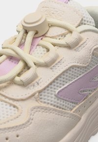 Detaljni prikaz bež i lavandaste tenisice s mrežastim panelima, antilop međunarodnim slojevima i elastičnim vezicama bez vezanja osiguranim plastičnim kopčom.