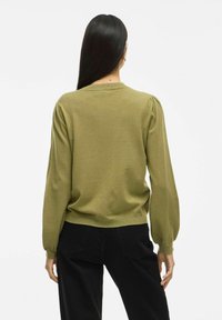 Olijfgroen pullover truien met ballonmouwen, geribbelde manchetten en zoom. Zachte textuur, achteraanzicht, gecombineerd met zwarte broeken. Eenvoudig ontwerp.