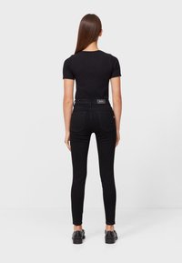 Jeans negros ajustados con cintura alta, cinco bolsillos y una textura suave. Combinados con una blusa negra de manga corta y zapatos negros.