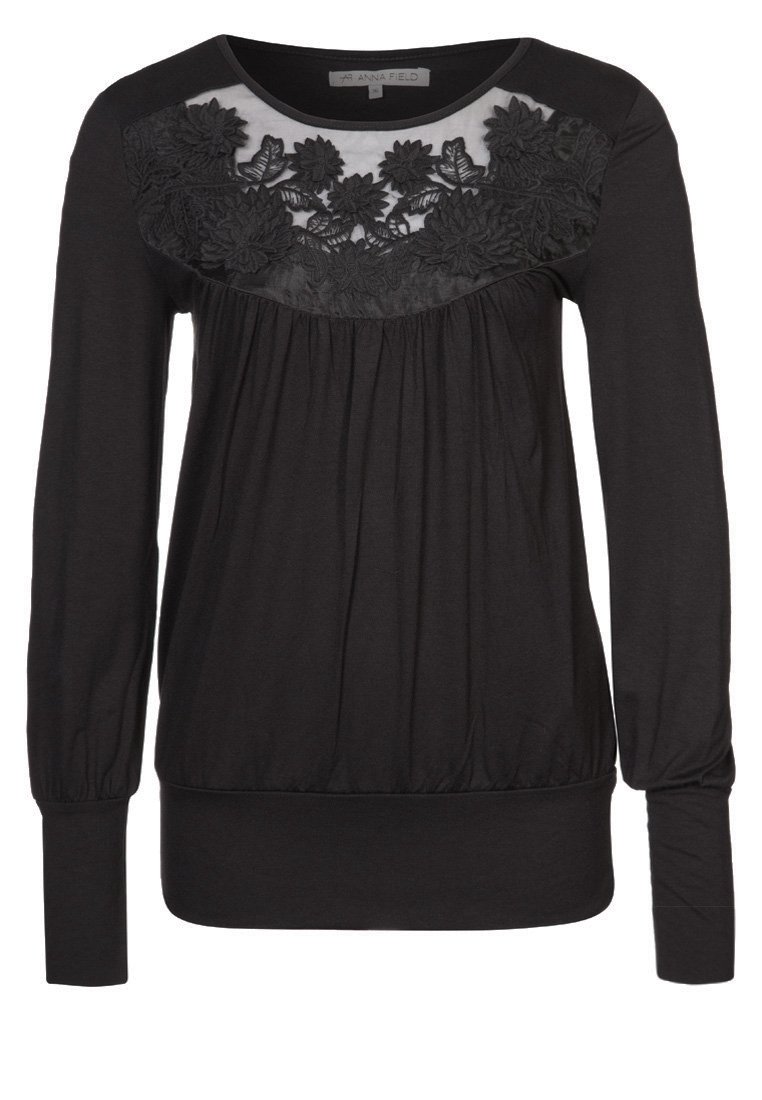 Svart långärmad överdel med ett strukturerat blommönstrat spetsfält över bröstet, samlad tyg under bysten och åtsittande ärmslut.
