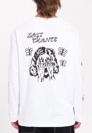 Camiseta de manga larga blanca con un gráfico en negro de una figura con las manos en la cara, rodeada de mariposas y el texto "ÚLTIMA OPORTUNIDAD."