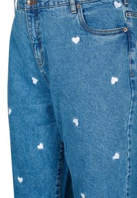 Gai zila džinsu bikses ar maziem baltajiem sirds rakstiem, kas izkaisīti visā audumā. Redzama šūšana un priekšējā kabata.