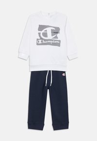 Hvid sweatshirt med grå Champion-logo, lange ærmer og ribbede manchetter; parret med marineblå sweatpants med et logo-patch og snøre.