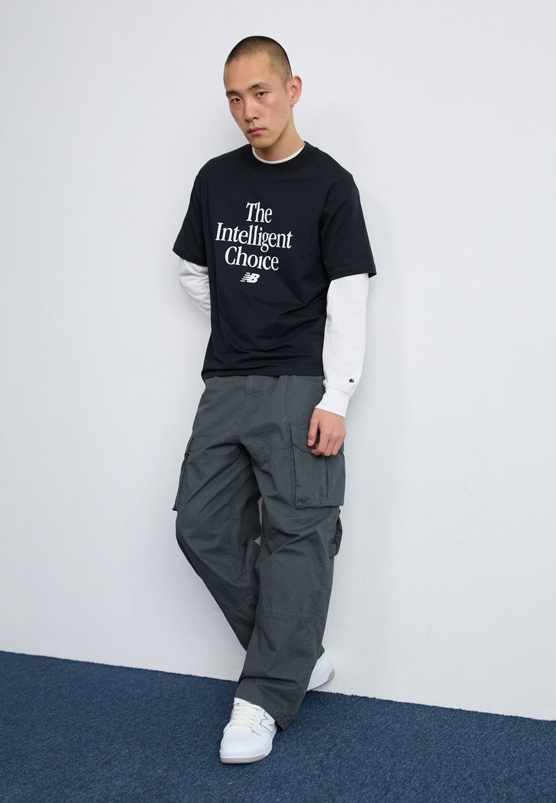 Schwarzes Baumwoll-T-Shirt mit weißem Text "Die intelligente Wahl", kombiniert mit dunkelgrauen Cargo-Hosen. Weiße Sneakers, strukturierte Stoffdetails.