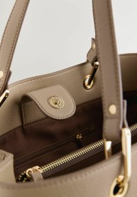 Beige Handtasche mit einer strukturierten Lederaußenseite, goldfarbenen Beschlägen, einem Reißverschluss oben und einem innen mit Stoff gefütterten Bereich, der über eine Reißverschlusstasche verfügt.