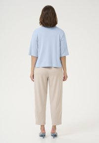 Light blue short-sleeve top with a round neckline, paired with beige tailored pants. The outfit features block colors and smooth textures.
