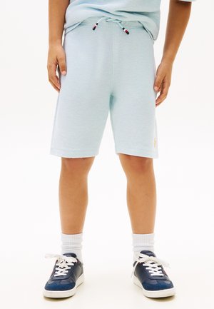 Kind draagt lichtblauwe korte broek met trekkoord, witte sokken en marineblauwe sneakers, staat met ontspannen handen langs het lichaam.