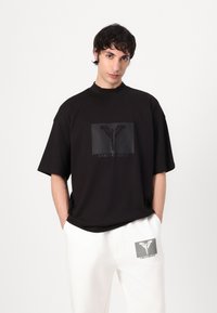 Zwarte katoenen t-shirt met een hoge halslijn, voorzien van een getextureerd grafisch vierkant en logo in een contrasterende kleur. Ontspannen pasvorm, korte mouwen.