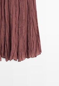 Tissu plissé mauve avec des plis verticaux et une texture légèrement transparente, suspendu librement sur un fond blanc.