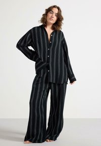 Set di pigiama rayato nero realizzato in morbido tessuto; include una camicia a maniche lunghe con bottoni e pantaloni larghi con righe bianche verticali.