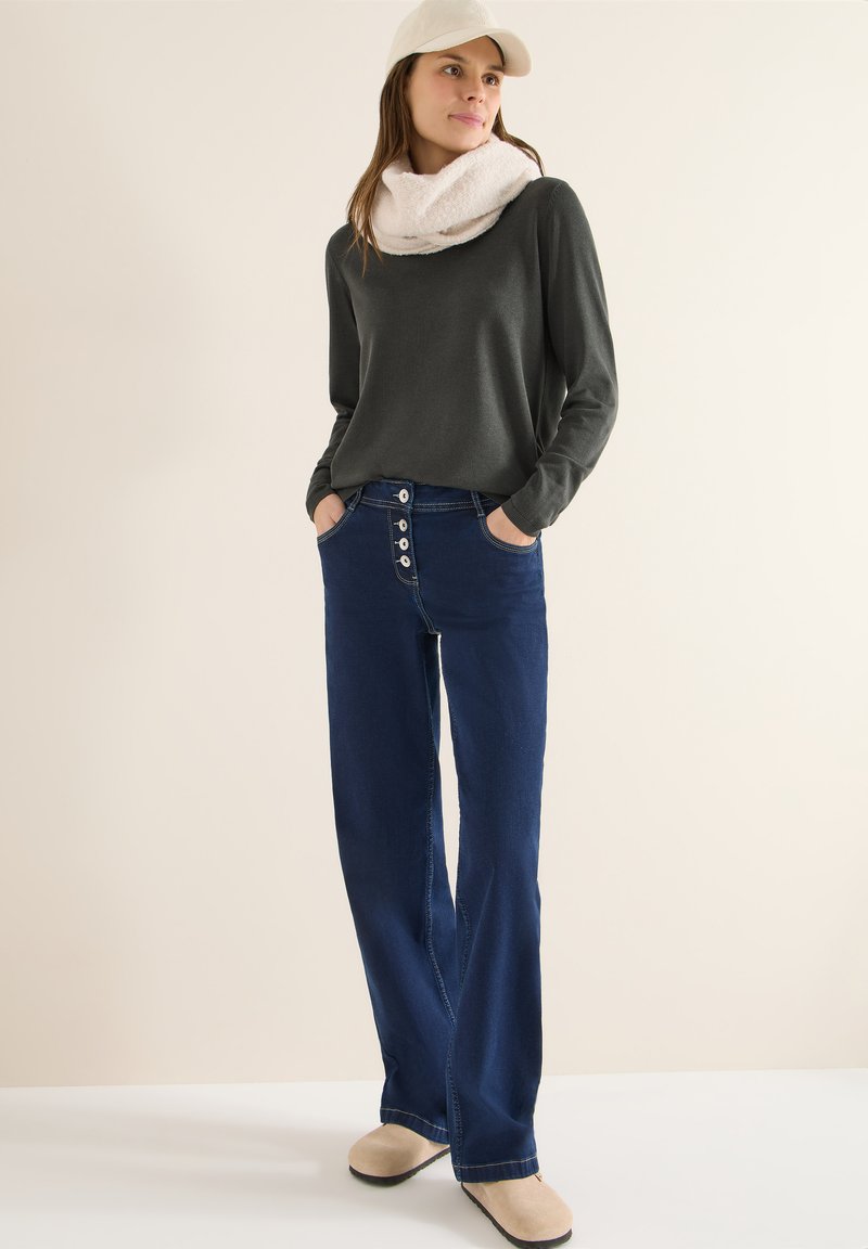 Ciemnoszara koszula z długim rękawem, jasnobeżowy szalik, niebieskie, wysokowzsitowe dżinsy z guzikami oraz beżowe buty. Prosty design i luźny krój.