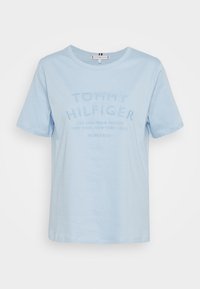 Vaaleansininen puuvillainen t-paita, jossa on lyhyet hihat ja kohopainettu "TOMMY HILFIGER" -teksti ja logo. Klassinen pyöreä kaula-aukko.