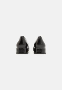 Scarpe in pelle nera con una finitura liscia, tacco quadrato basso e design a punta, viste da dietro con uno stile minimalista.