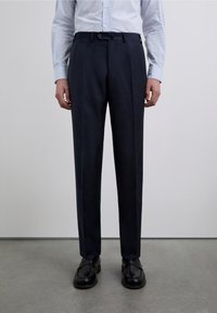 Pantalones entallados azul marino con frente plano, trabillas para cinturón y ajuste ajustado. Confeccionados en tela suave, con textura sutil y raya marcada.