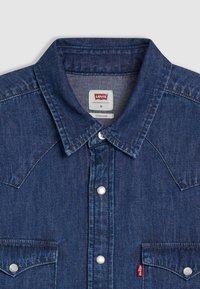 Σκούρο μπλε πουκάμισο από τζιν με μυτερό γιακά, κουμπιά τύπου snap και δύο τσέπες στο στήθος. Διαθέτει ετικέτα Levi's στο εσωτερικό του γιακά.