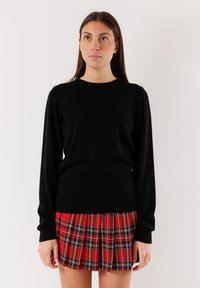 Maglione nero lavorato a maglia con maniche lunghe e scollatura rotonda, abbinato a una gonna plissettata a quadri rossi con accenti blu e gialli.