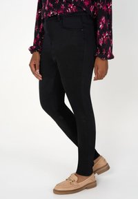 Leggings en denim noir au design ajusté. Texture lisse, taille haute et coutures latérales visibles. Associés à des mocassins de couleur claire.