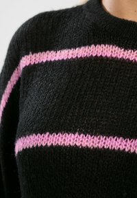 Czarny sweter robiony na drutach z poziomymi paskami różowej włóczki na klatce piersiowej. Strukturalny splot z okrągłym dekoltem.