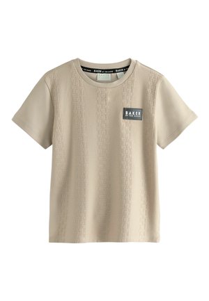 Beige lyhythihainen T-paita, joka on tehty sileästä kankaasta. Siinä on teksturoitu kuvio ja musta logopatchi rinnassa. Pyöreä kaula-aukkotyyli.