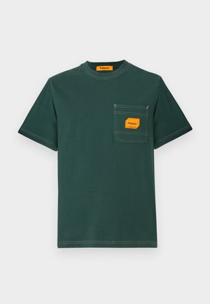 Grøn bomuld t-shirt med rund hals, korte ærmer og en forlomma med en orange etiket. Kontrastsyning er synlig.