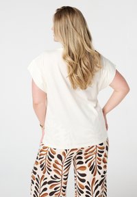 Haut créme à manches courtes avec une coupe décontractée, associé à un pantalon à jambes larges présentant un motif de feuilles brun et noir. Texture de tissu douce.