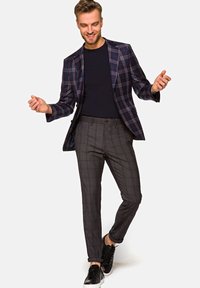 Granatowa marynarka w kratę o dopasowanym kroju, zestawiona z szarymi spodniami w kratę. Czarne sneakersy dopełniają całość, prezentując nowoczesny casualowy styl.