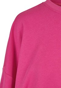 Gros plan d'un pull rose vif à col rond montrant l'épaule et la partie supérieure de la poitrine avec une texture tricotée visible.