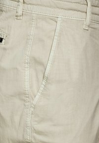 Béžové bavlněné kalhoty s hladkým povrchem, strukturovanými kapsami s viditelným švem a čistým, upraveným designem.