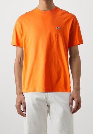 Oranges Baumwoll-T-Shirt mit rundem Halsausschnitt und kurzen Ärmeln, ausgestattet mit einem kleinen grünen Lacoste-Logo auf der linken Brust.