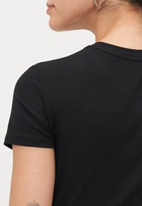 Zwarte geribde t-shirt met korte mouwen, zichtbare nekdetails en een gestructureerde stof. Minimalistisch ontwerp zonder opvallende patronen of accenten.