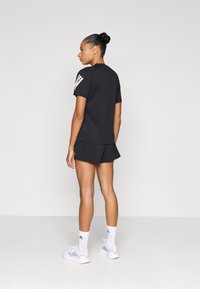 Czarny sportowy t-shirt z krótkimi r ękawami i białymi paskami na ramionach, w połączeniu z czarną spódniczką sportową (skort). Białe trampki z różowymi akcentami.